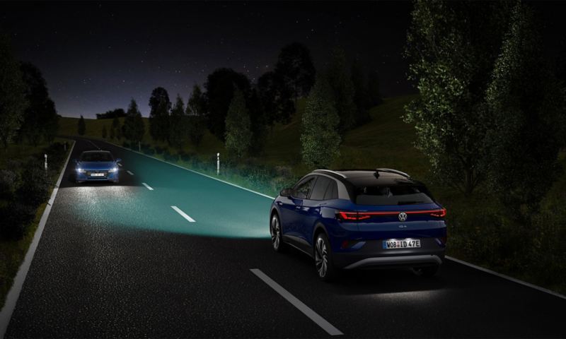 Une VW ID.4 bleu, phares allumés, roule de nuit sur une route.