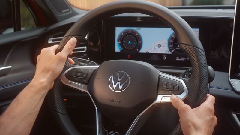 Detailed view of the cockpit in a VW Tiguan. Two hands clasp the steering wheel.