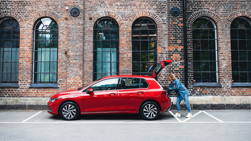 Eine Frau steht an der geöffneten Heckklappe eines roten VW Golf.