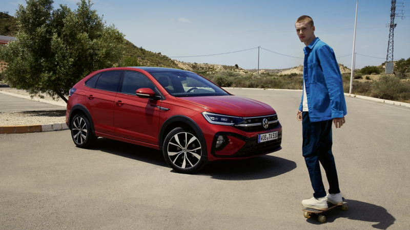 Ein Mann fährt auf einem Skateboard vor einem geparkten VW Taigo entlang.