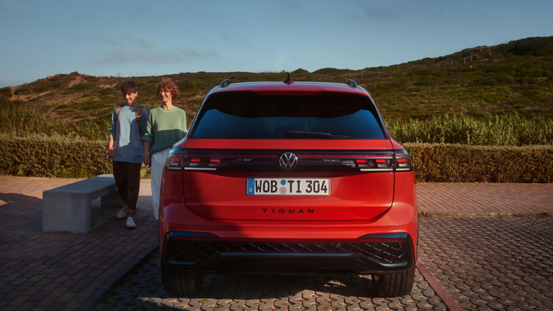 A man and woman standing beside their red Plug-in hybrid vehicle