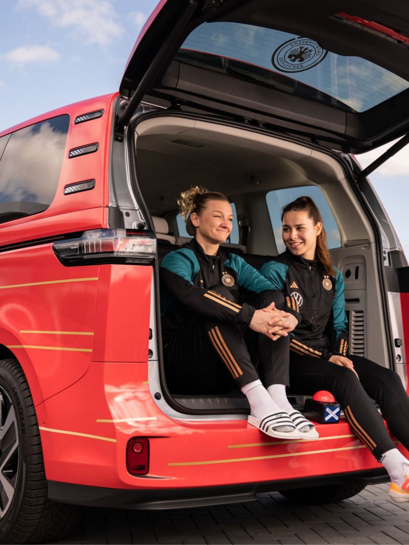 Zwei DFB Spielerinnen sitzen im Kofferraum bei geöffneten Heckklappe.