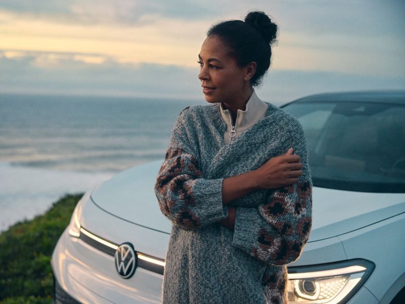 Eine Frau steht vor einem weißen VW. Im Hintergrund ist weite Landschaft zu sehen.