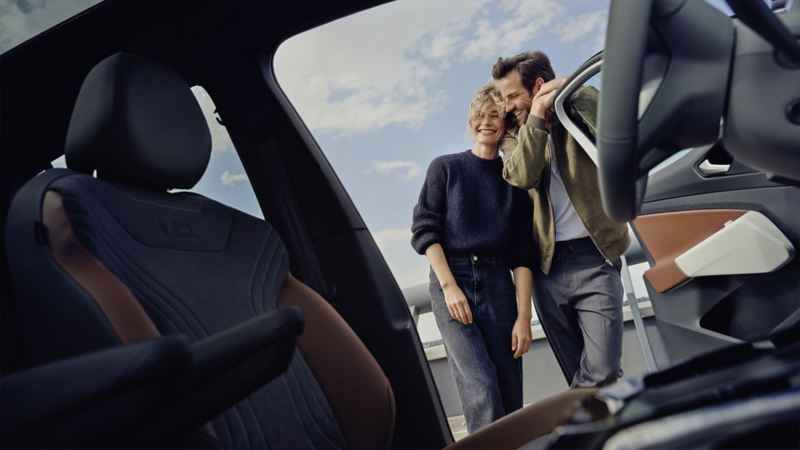 Ein Paar steht aneinander angelehnt an der offenen Fahrertür eines VW.
