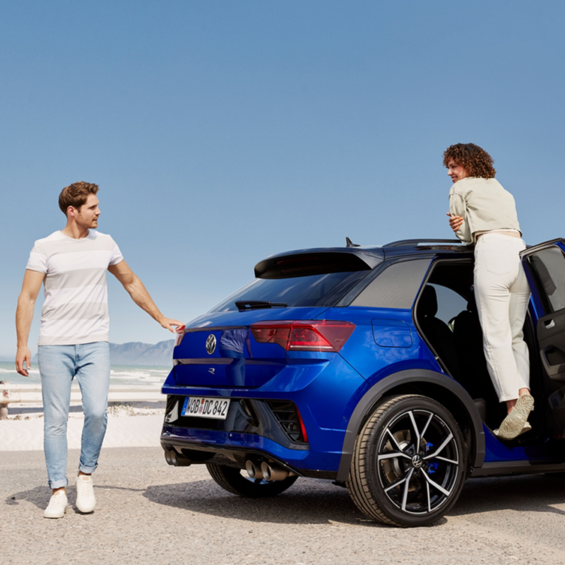 Una pareja al lado de un Volkswagen T-Roc R de color azul oscuro estacionado