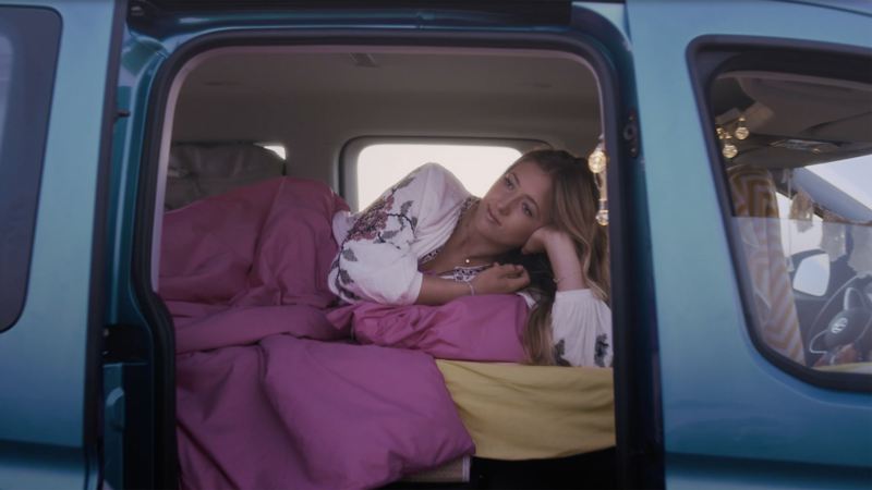 Person looking out sliding door of Volkswagen Caddy California while lying in bed.