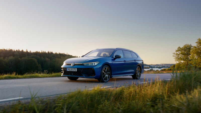 En blå VW Passat kör längs sommarväg i gryningsljus
