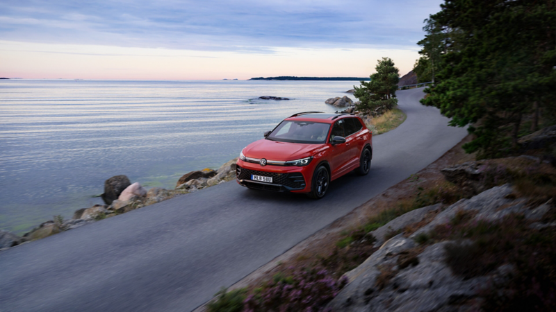 Röd laddbar Tiguan kör längs en kurvig väg med havet precis intill