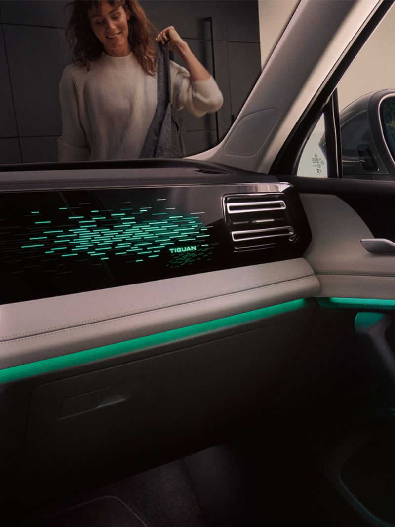Vue intérieure du VW Tiguan de nuit, l’écran couleur affiche les réglages de l’éclairage d’ambiance optionnel, l’intérieur est éclairé en vert.