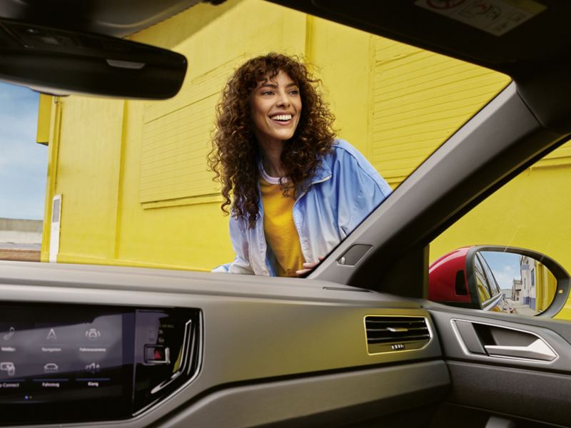 Eine Frau ist durch eine Frontscheibe aus dem Innenraum eines VW zu sehen.