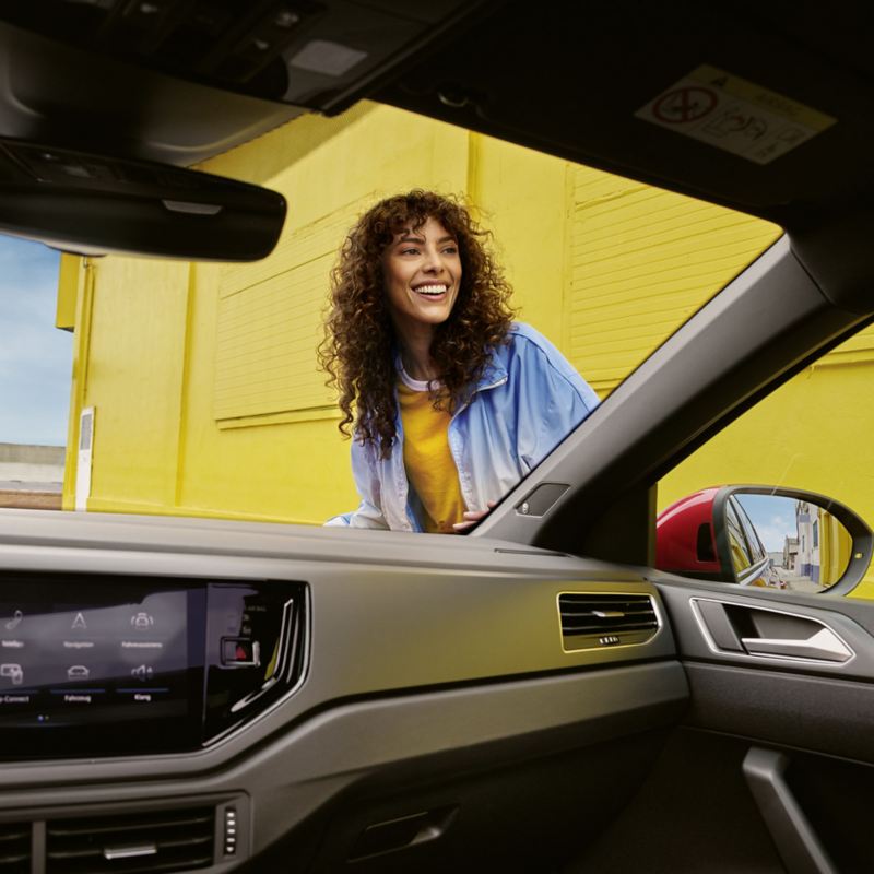 Eine Frau ist durch eine Frontscheibe aus dem Innenraum eines VW zu sehen.
