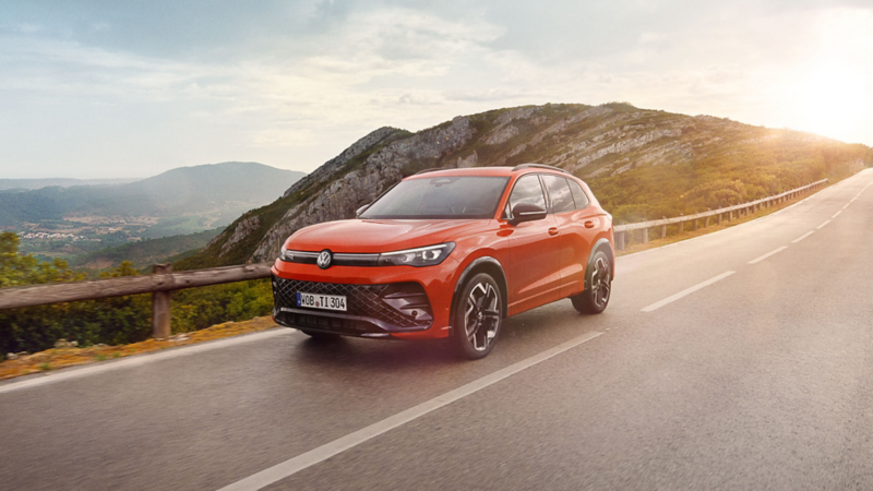 Frontansicht eines roten VW Tiguan auf einer bergigen Landstraße bei Sonnenuntergang.