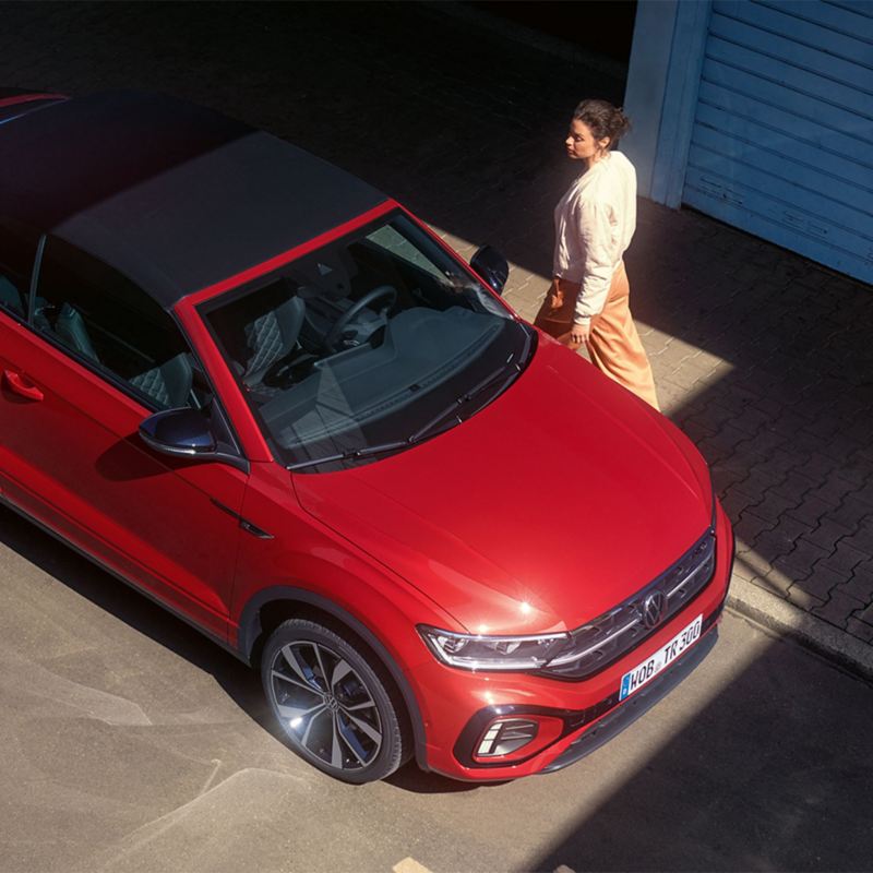 Eine Frau geht zur Fahrertür eines roten VW T-Roc Cabrio.
