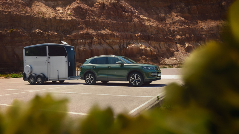 Dark green VW Tiguan with horse trailer parked in front of a rocky landscape.