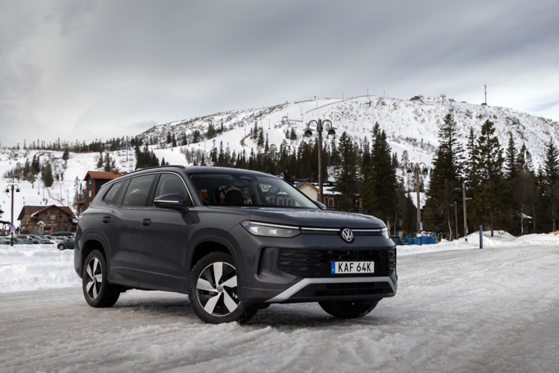 En svart Tayron parkerad med ett snötäckt berg i bagrunden. Sedd snett framifrån.