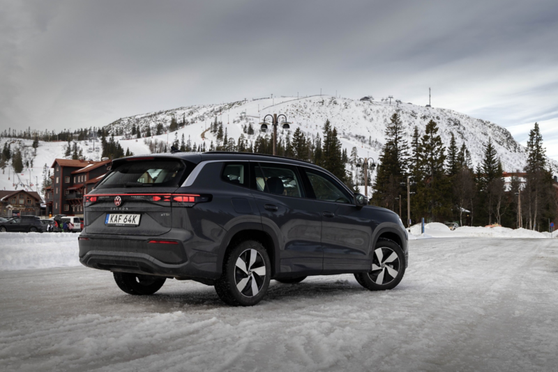 En svart Tayron parkerad med ett snötäckt berg i bagrunden. Sedd snett bakifrån.