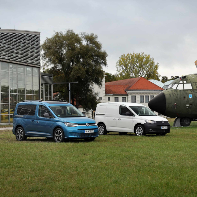 Un Nuovo Caddy Cargo e un Nuovo Caddy California Volkswagen parcheggiati in un prato.