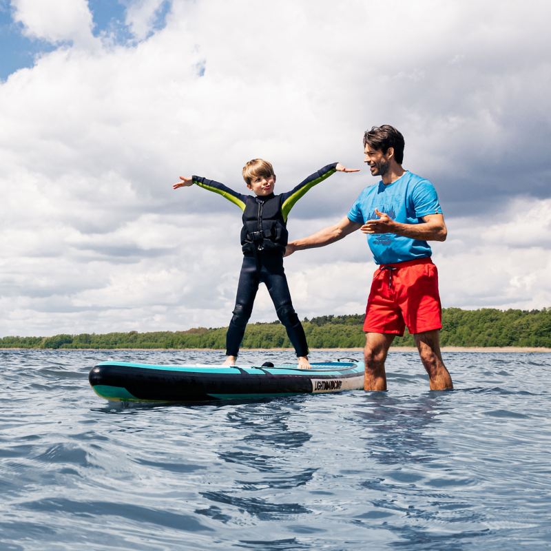Ein Kind steht stolz auf einem Stand-Up-Paddle Board neben seinem Vater