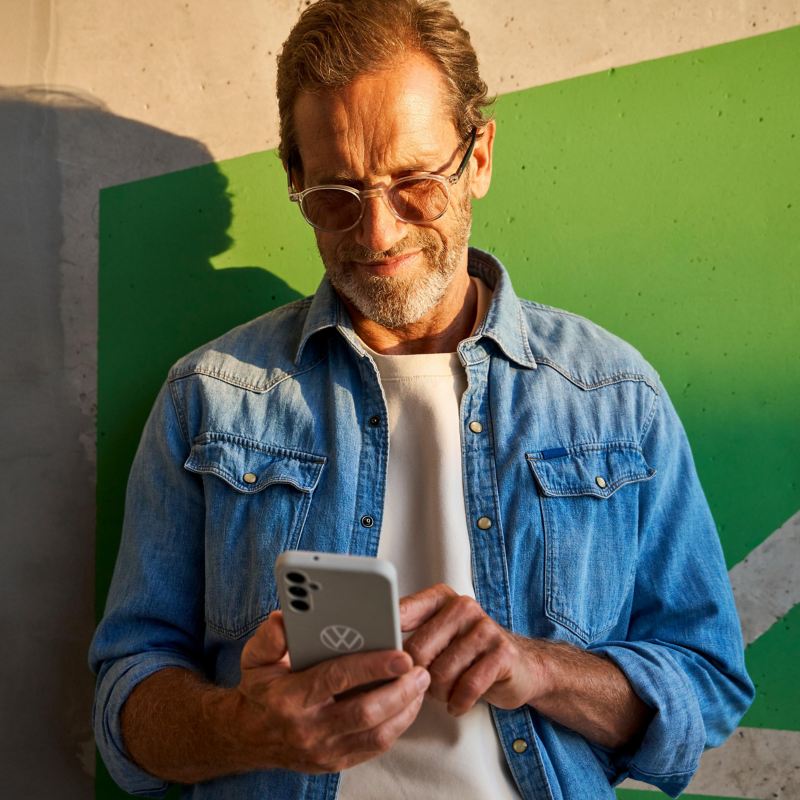 Man leaning against a wall and books Driving Experience appointment on his smartphone