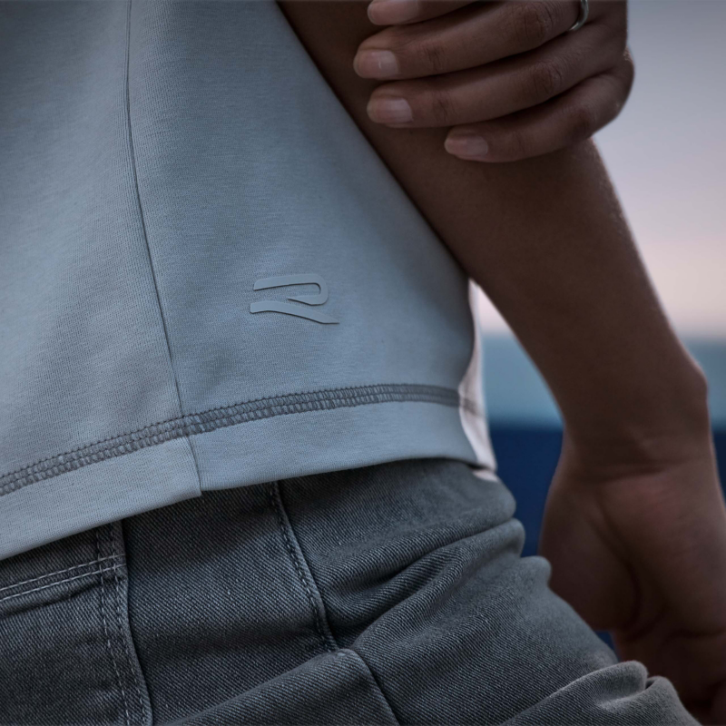 Blick von der Seite auf T-Shirt, im Fokus der Saum mit R-Logo darüber