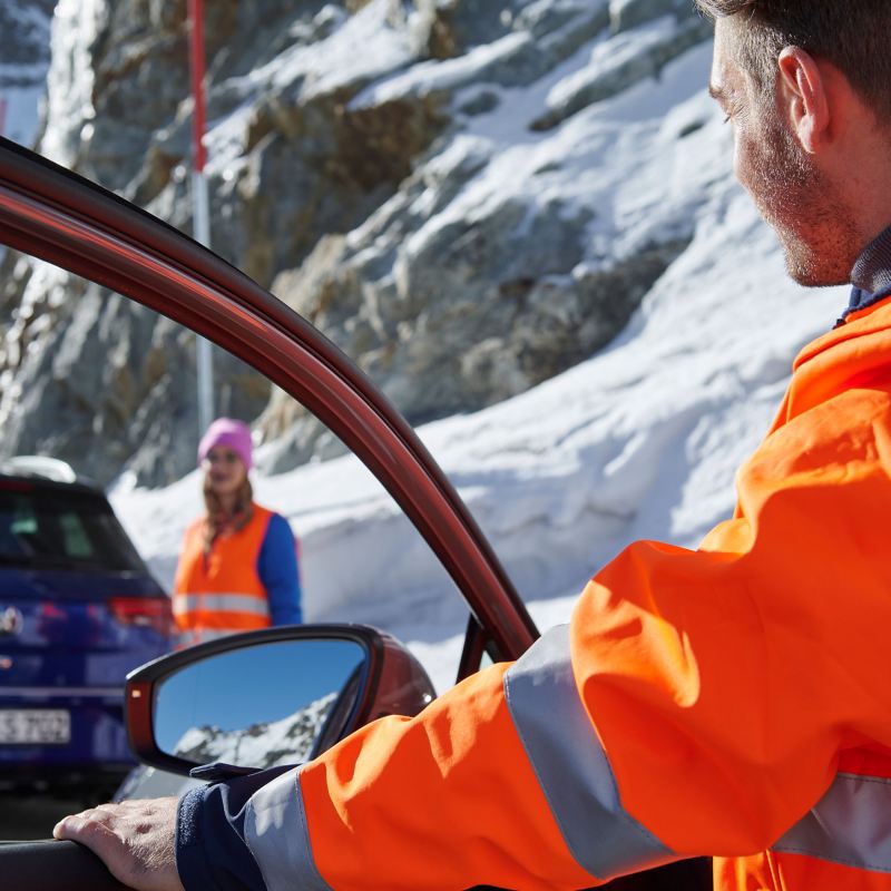 Volkswagen Notdienst – ein Servicemitarbeiter steht an der Fahrertür eines VW Autos, im Hintergrund verschneite Berge