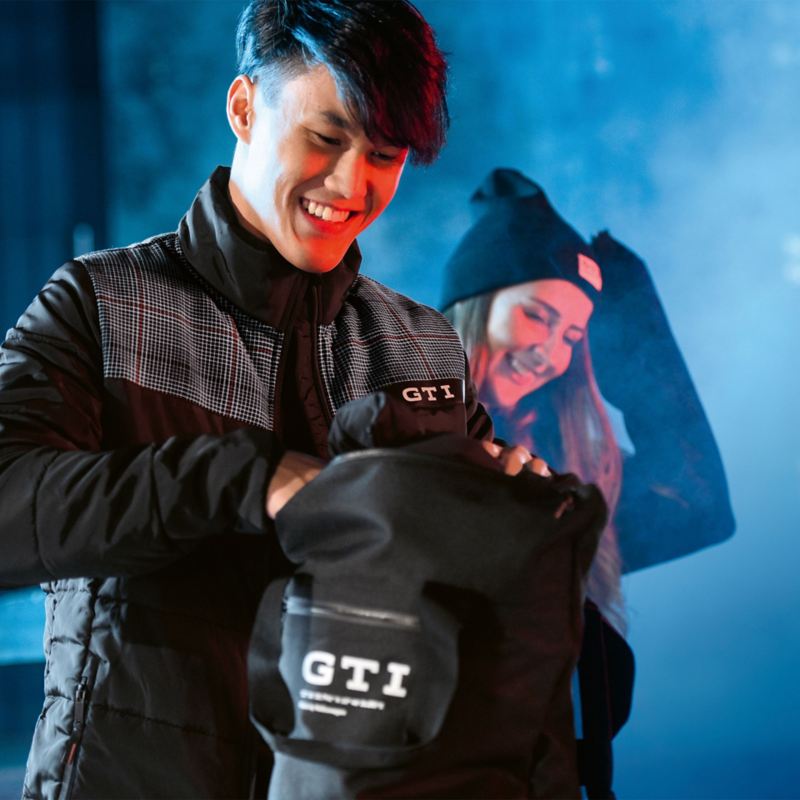 Una pareja riendo con un look GTI de moda, el hombre busca algo en su mochila GTI