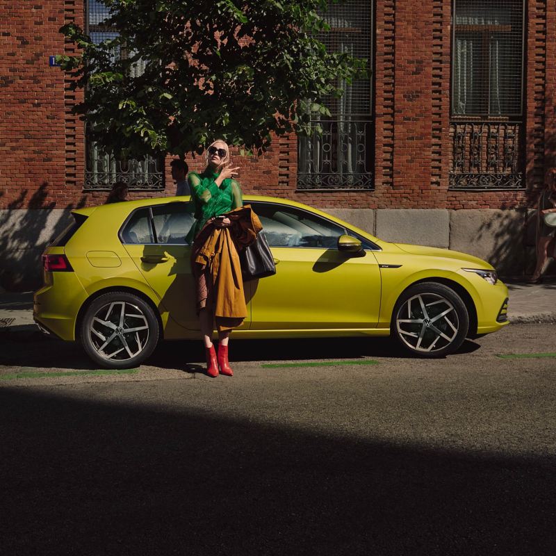 Una mujer elegantemente vestida delante de un Volkswagen Golf 8