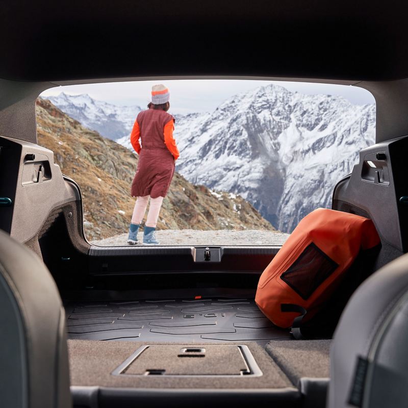 Blick durch den Kofferraum eines ID.3 zeigt eine Frau, die die Aussicht auf verschneite Berge genießt
