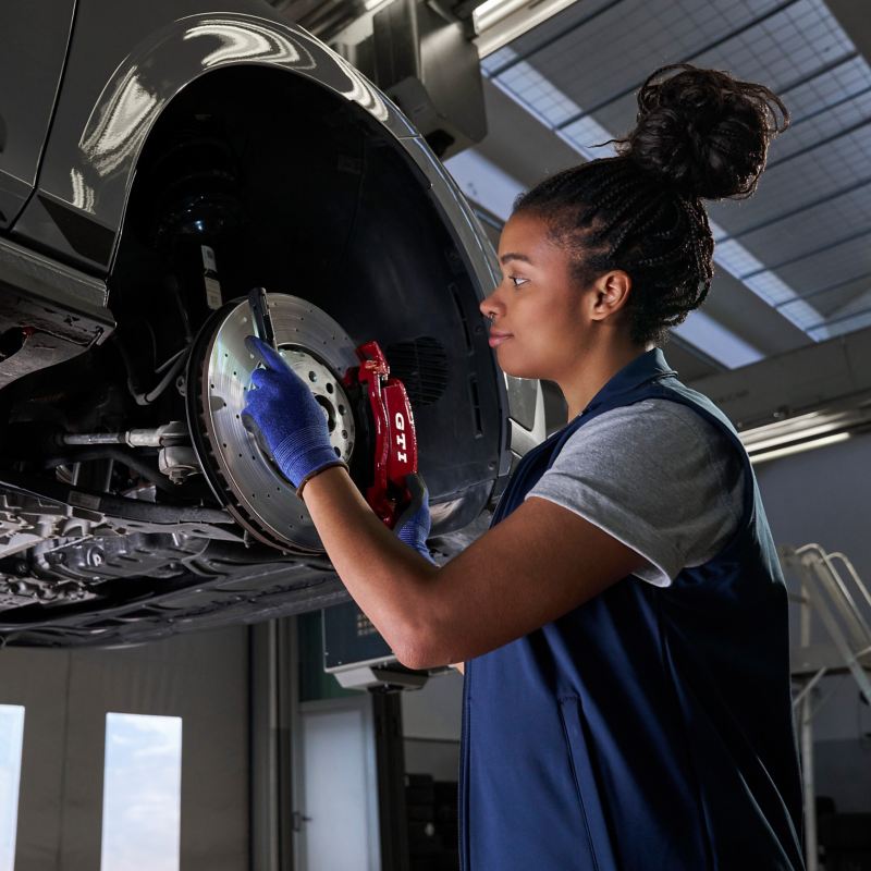 Une collaboratrice d’atelier Volkswagen inspecte le frein d’origine Volkswagen d’une Volkswagen GTI