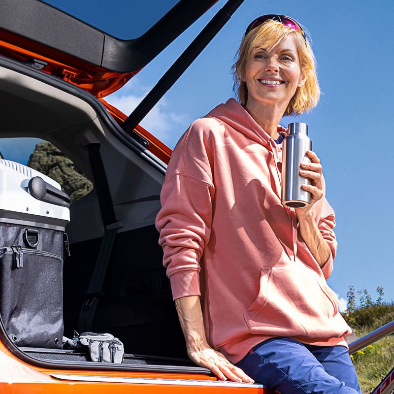 Eine Frau macht eine Pause neben ihrem Auto mit offenem Kofferraum mit praktischem VW Zubehör im Inneren