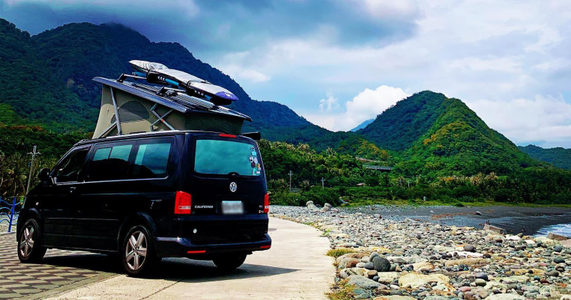 黑色California岸邊石頭地停車區，車頂帳掀起，車頂上方還架有衝浪板