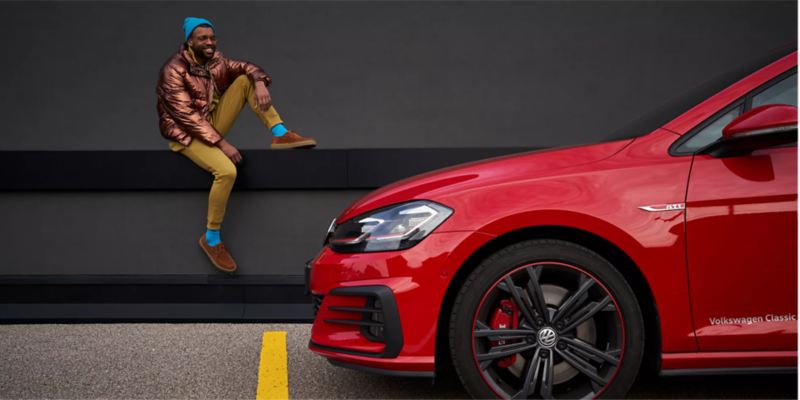 Un hombre elegante admirando el vehículo Volkswagen rojo.