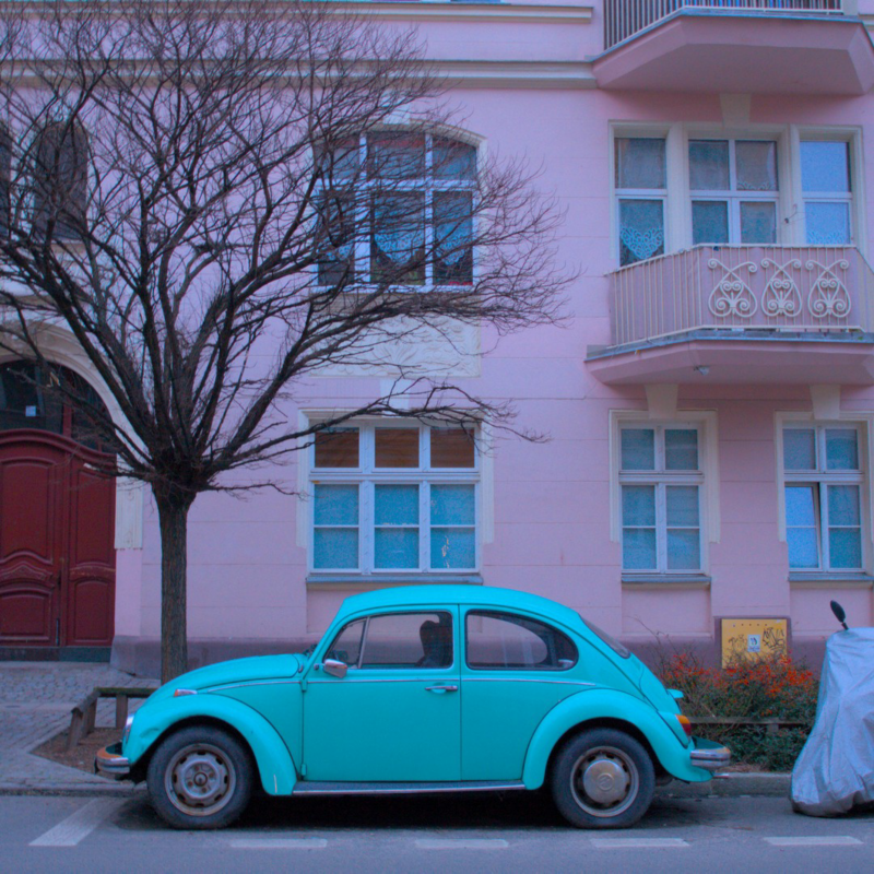 Turkusowy Volkswagen Beetle na tle różowej kamienicy. 