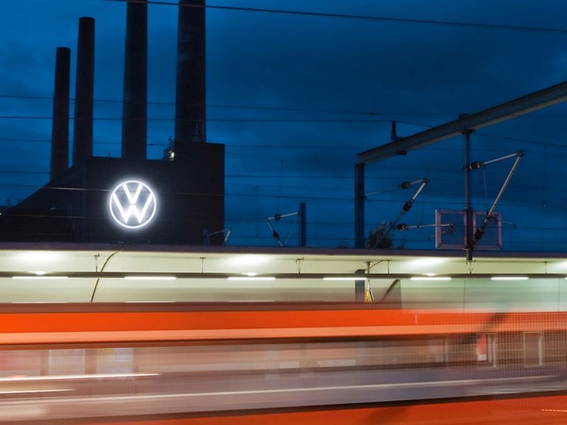 A moving train and the Volkswagen plant in Wolfsburg at night in the background
