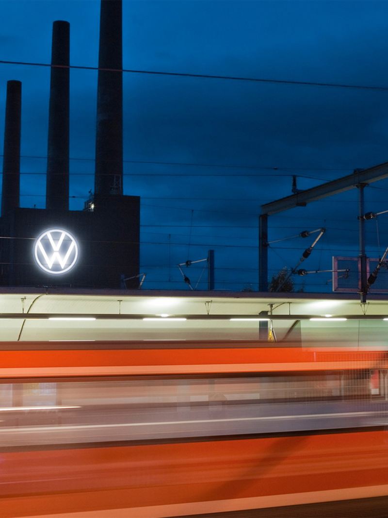 Ein fahrender Zug und im Hintergrund das Volkswagen Werk Wolfsburg bei Nacht