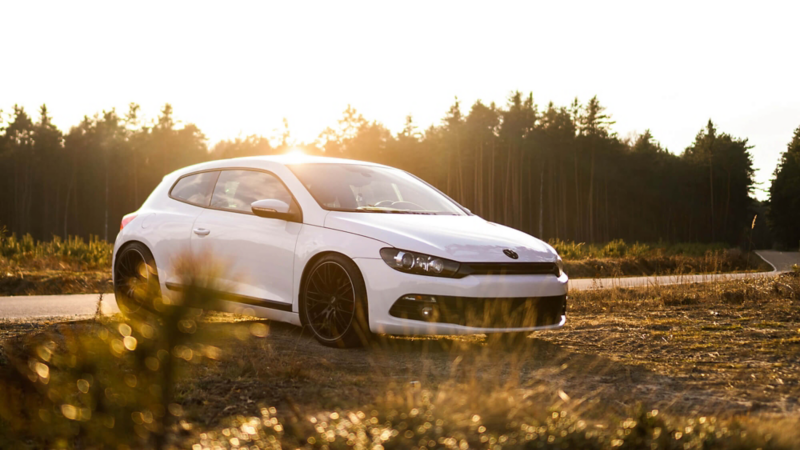 Biały samochód volkswagena na łące przy zachodzie słońca