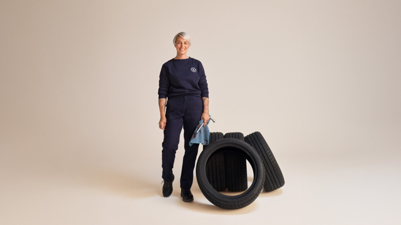 A Volkswagen service employee standing beside a pile of tires on a plain background