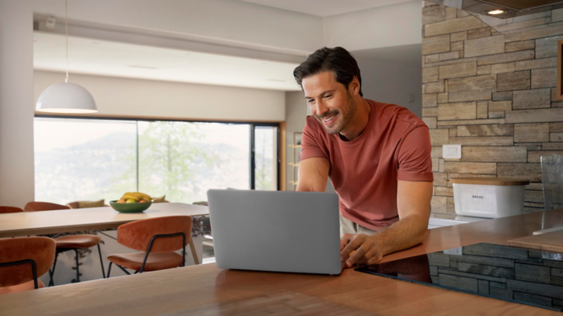Un hombre utilizando un ordenador portátil en una cocina con vistas al exterior.