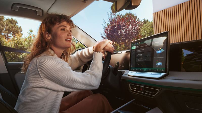 Jonge vrouw op de bestuurdersstoel van haar VW Tiguan in interactie met de digitale spraakassistent 