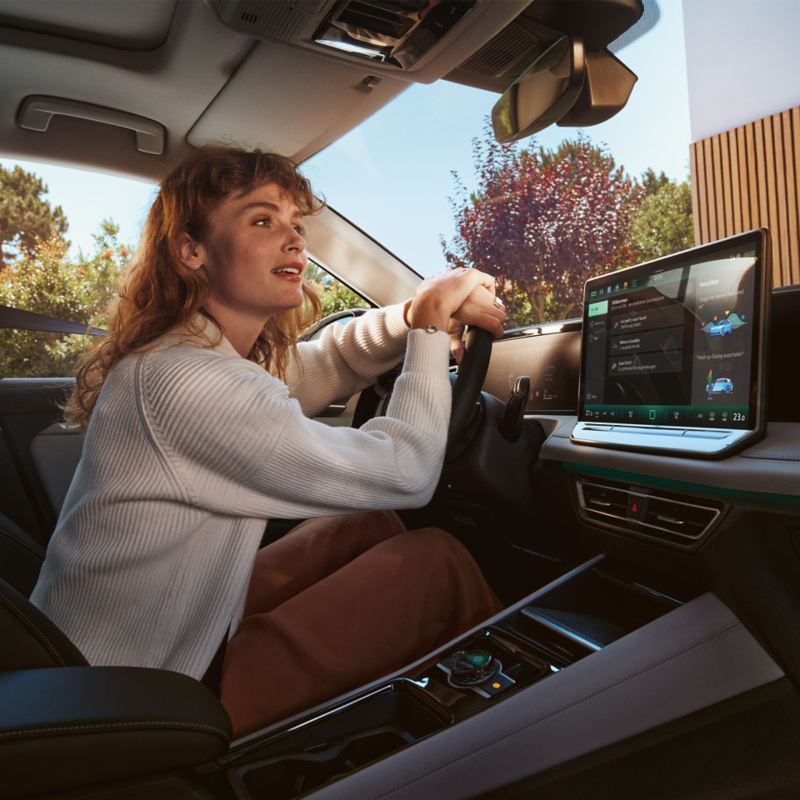 Junge Frau auf dem Fahrersitz ihres VW Tiguan in Interaktion mit dem digitalen Sprachassistenten 