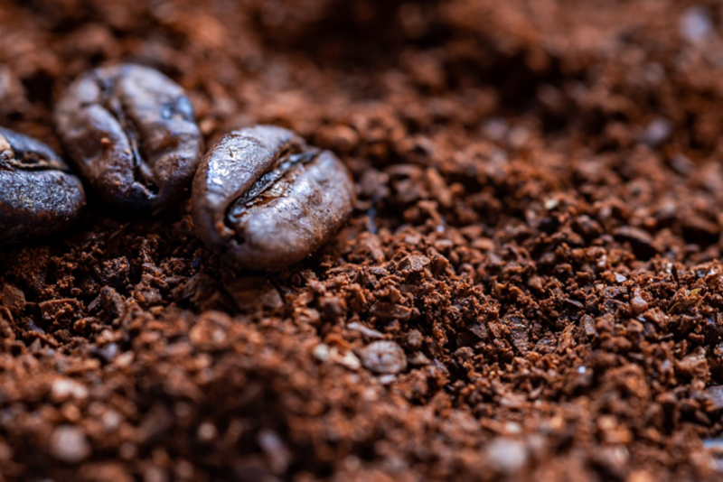 Two brown coffee beans sitting on top of a pile of ground coffee.