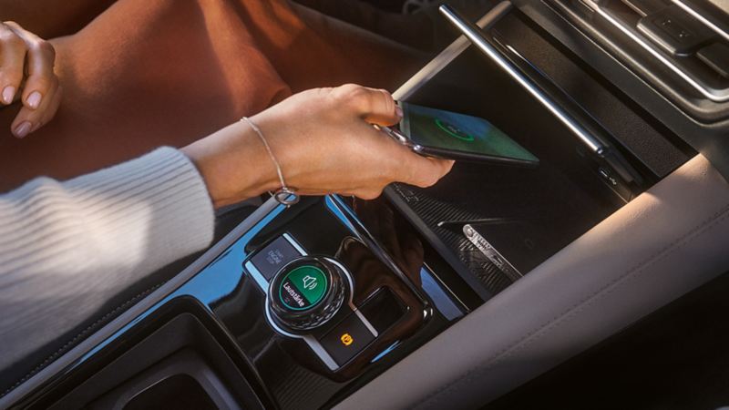 Vue détaillée de l'intérieur du VW Tiguan Une main ouvre un compartiment de rangement depuis le siège conducteur pour charger un téléphone portable par induction.