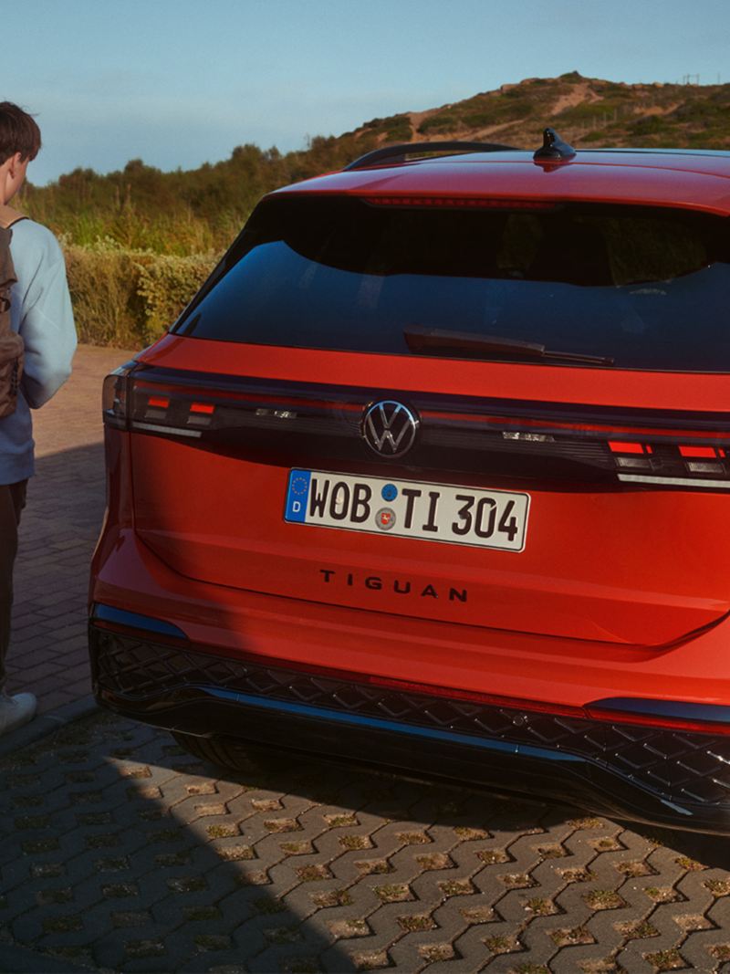 Tył zaparkowanego Volkswagena Tiguana. Kobieta i młody chłopak podchodzą do samochodu.