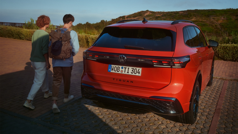 Tył zaparkowanego Volkswagena Tiguana. Kobieta i młody chłopak podchodzą do samochodu.