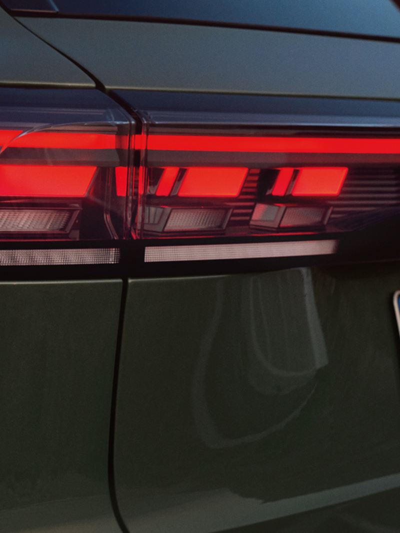 Vue détaillée de la signature lumineuse arrière d’un VW Tiguan vert foncé garé devant un paysage rocheux.
