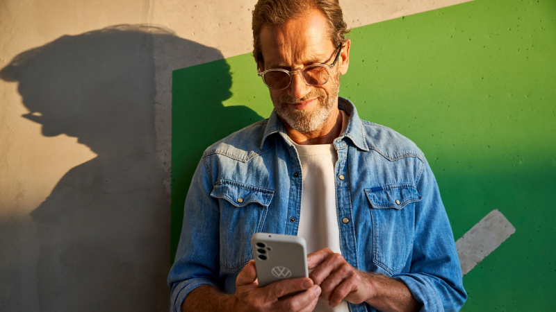 Mann mit Sonnenbrille tippt auf sein Smartphone – im Hintergrund eine grüne Wand