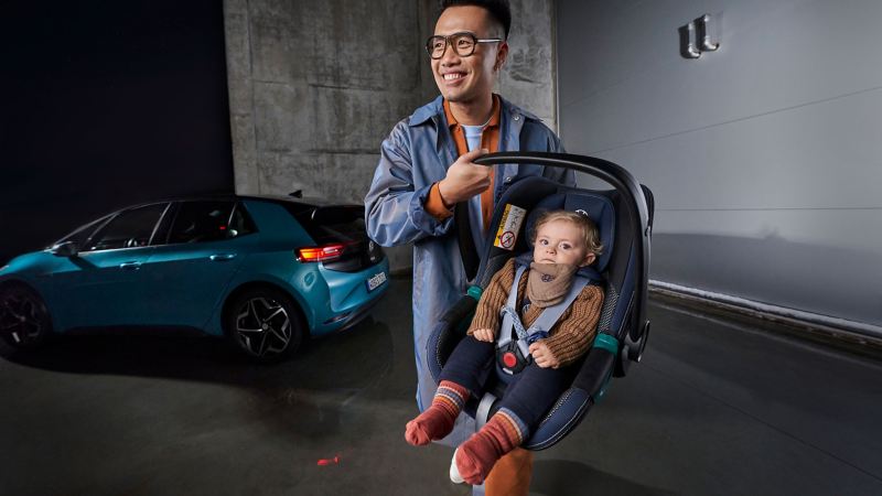 Ένας νεαρός πατέρας μεταφέρει το παιδί του σε ένα παιδικό κάθισμα από τα Αξεσουάρ VW