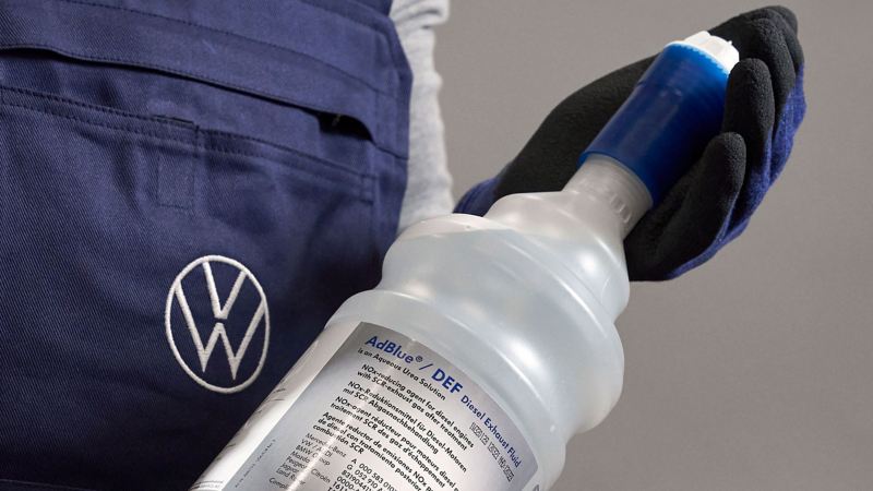 Detailed view of a VW service employee holding an AdBlue® bottle
