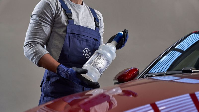 A VW service employee is cleaning the exterior of a VW car – care products