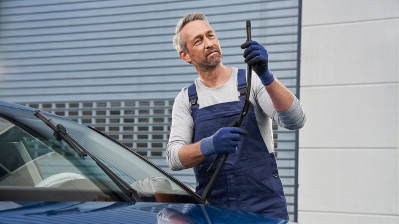 Un empleado del servicio técnico de VW revisa los limpiaparabrisas de un VW azul – limpiaparabrisas Aero